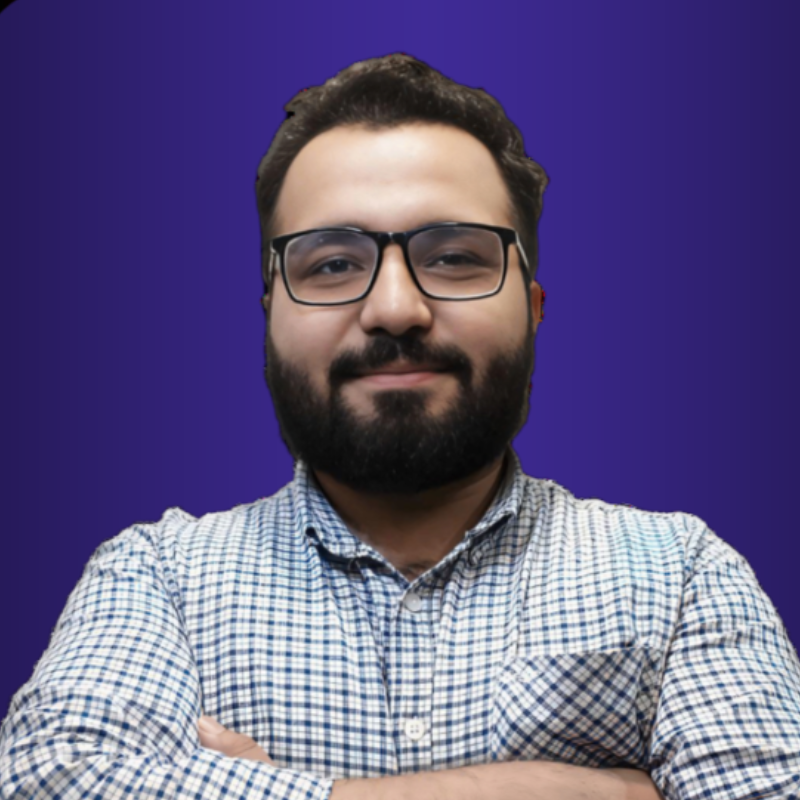 A man with glasses and beard standing in front of a blue background.